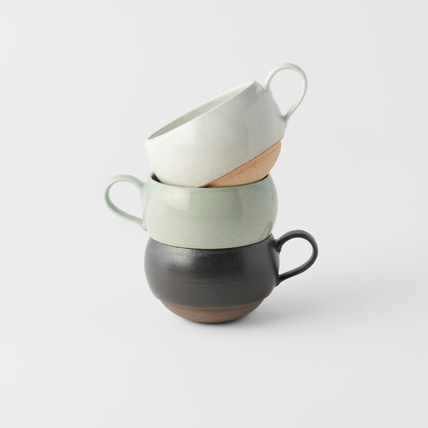 Stacked ceramic sphere mugs in black, green, and cream colors, showcasing artisanal craftsmanship.