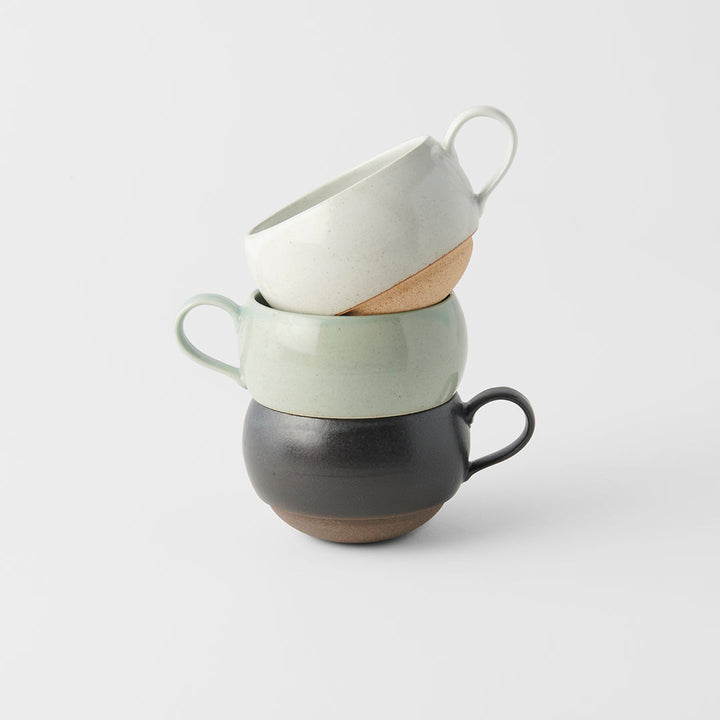 Stacked ceramic sphere mugs in black, green, and cream colors, showcasing artisanal craftsmanship.