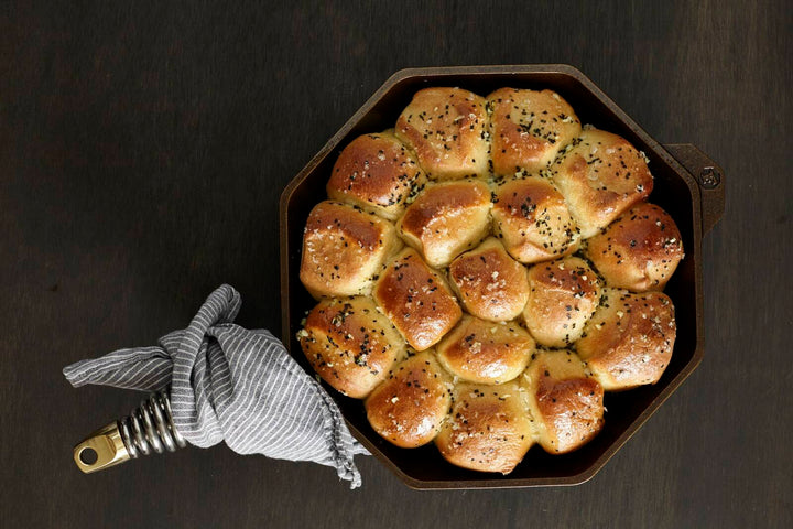 Golden baked rolls in a FINEX cast iron skillet with a patterned cloth, showcasing the skillet's octagonal design.