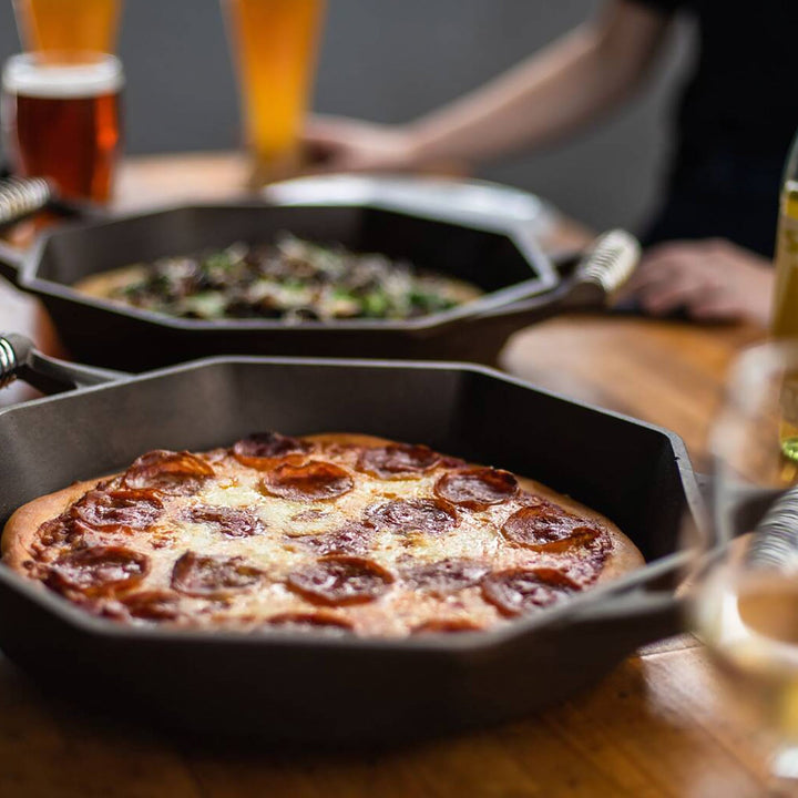 FINEX cast iron skillet with pepperoni pizza, showcasing octagonal design and polished surface on a wooden table.