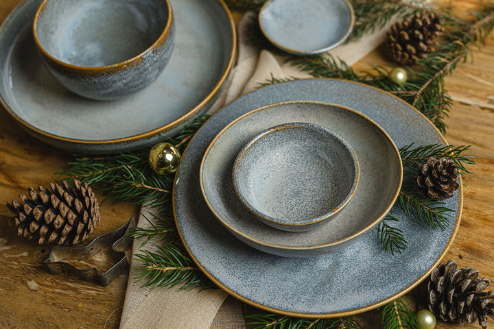 Oval 19cm bowl in steel grey glaze with organic shape, surrounded by pinecones and greenery on wooden table.