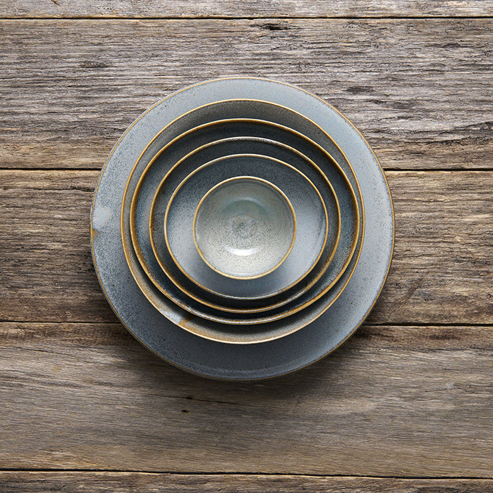 Stack of five steel grey glazed bowls with subtle speckling and earthy brown edges on a wooden surface.