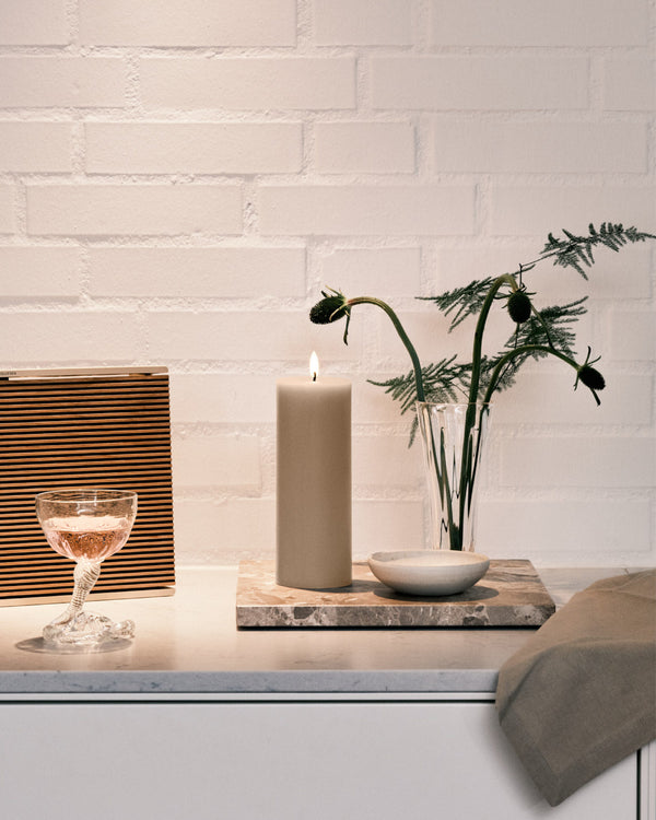 Ester & Erik LED pillar candle glowing on a stylish table with a glass of rose and greenery in a modern decor setting.