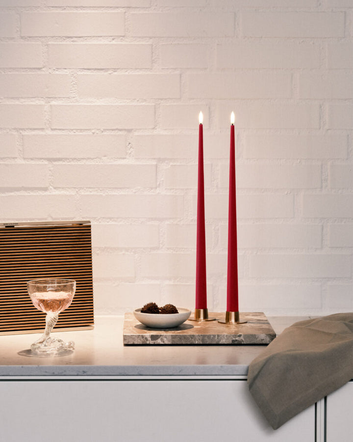 Elegant Ester & Erik LED taper candles in red, illuminating a modern table setting with snacks and drinks.