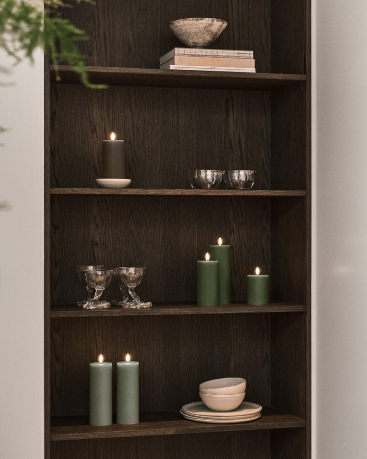 LED pillar candles in green and black on a wooden shelf, creating a cozy and inviting ambiance.
