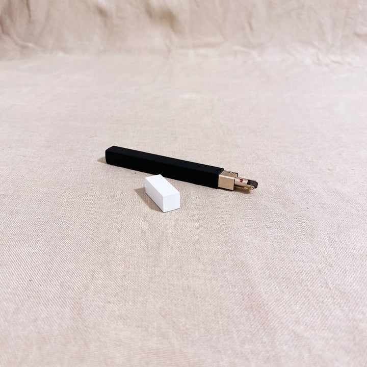 Tsubota Pearl Queue matte black and white petrol lighter resting on fabric background.