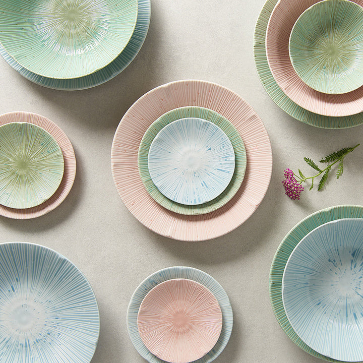 Colorful collection of textured ceramic plates and bowls in pastel blue, green, and pink, arranged elegantly on a surface.