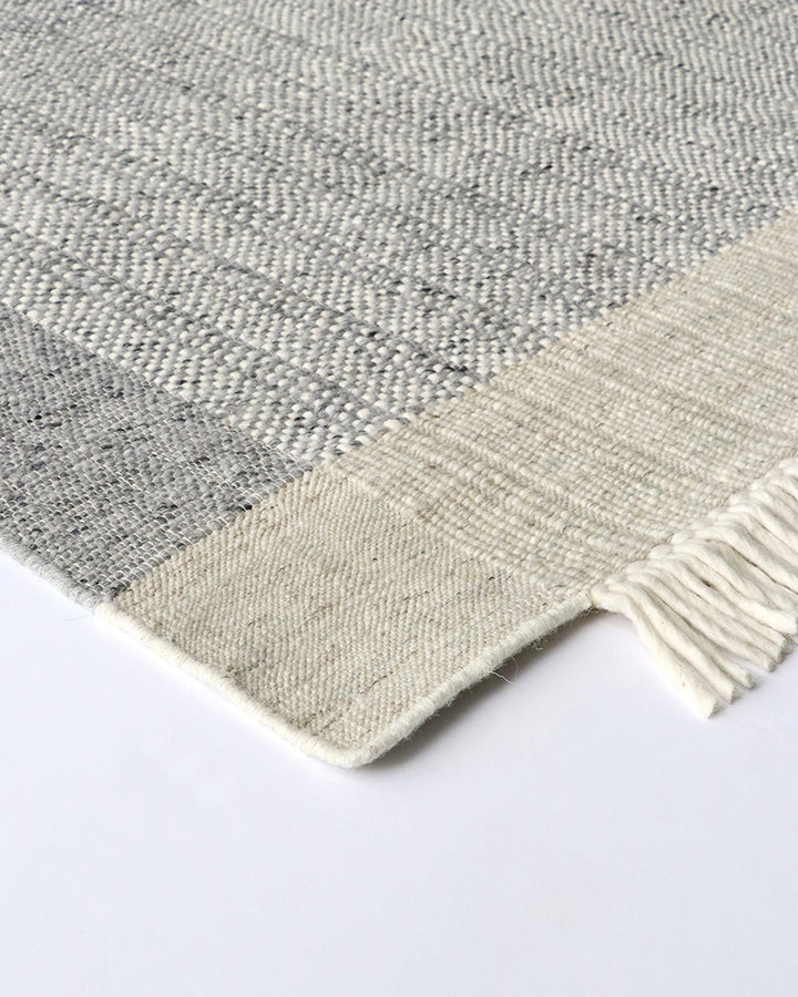 Lindis Floor Rug Add understated chic to your interior with the exceptional design of our Lindis floor rug. Handwoven by skilled artisans, tonal fibres are woven in a classic 1-1 structure, creating a refined and interesting border design. Fringing on bot