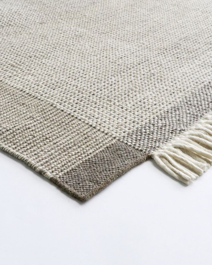 Lindis Floor Rug Add understated chic to your interior with the exceptional design of our Lindis floor rug. Handwoven by skilled artisans, tonal fibres are woven in a classic 1-1 structure, creating a refined and interesting border design. Fringing on bot