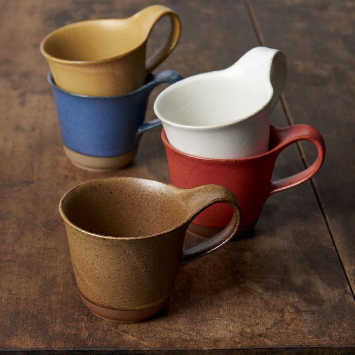 Four ceramic mugs in various colors including brown, blue, red, and white, on a wooden surface.